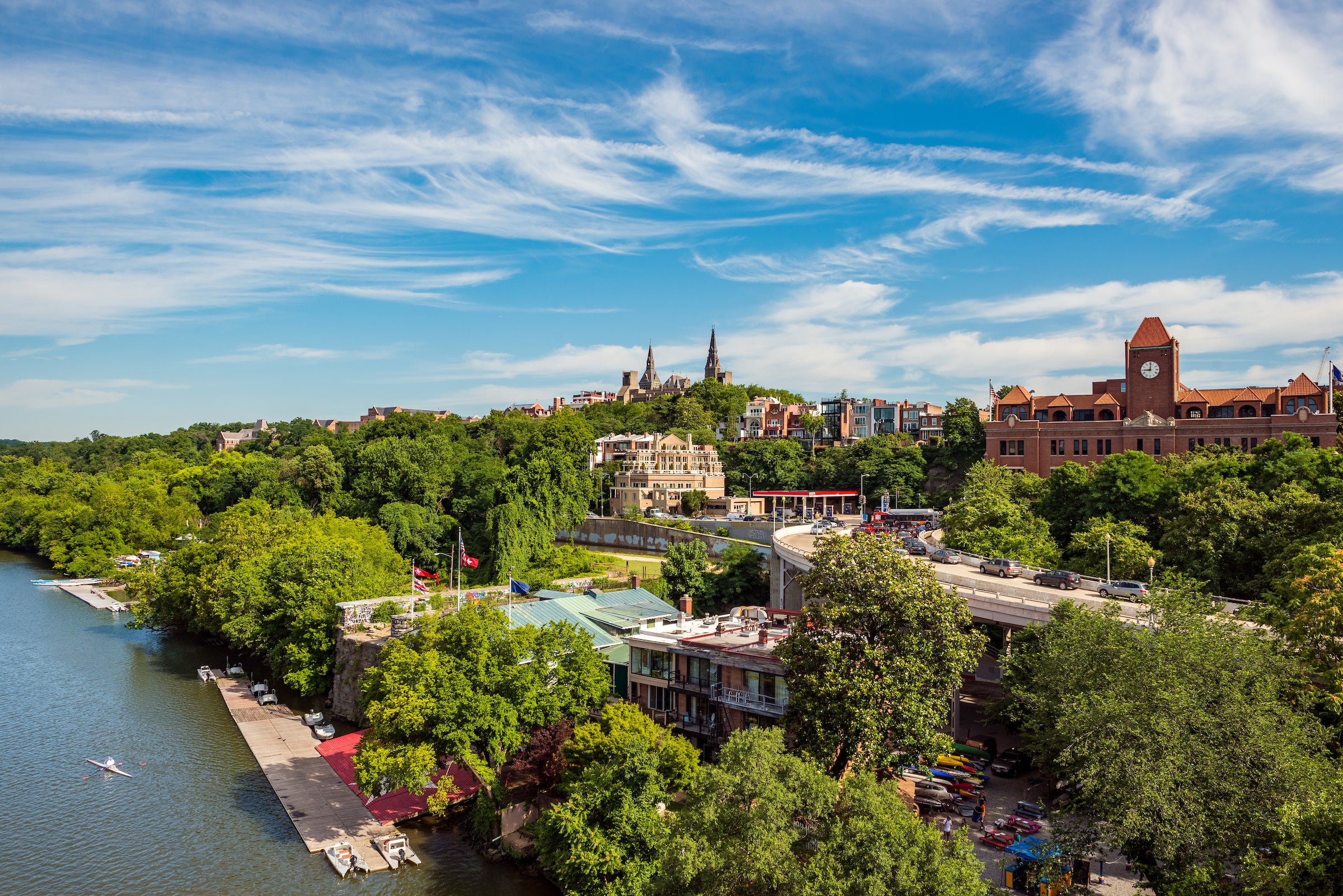 Trees and the skyline of Georgetown next to the Potomac River on a sunny day with some clouds