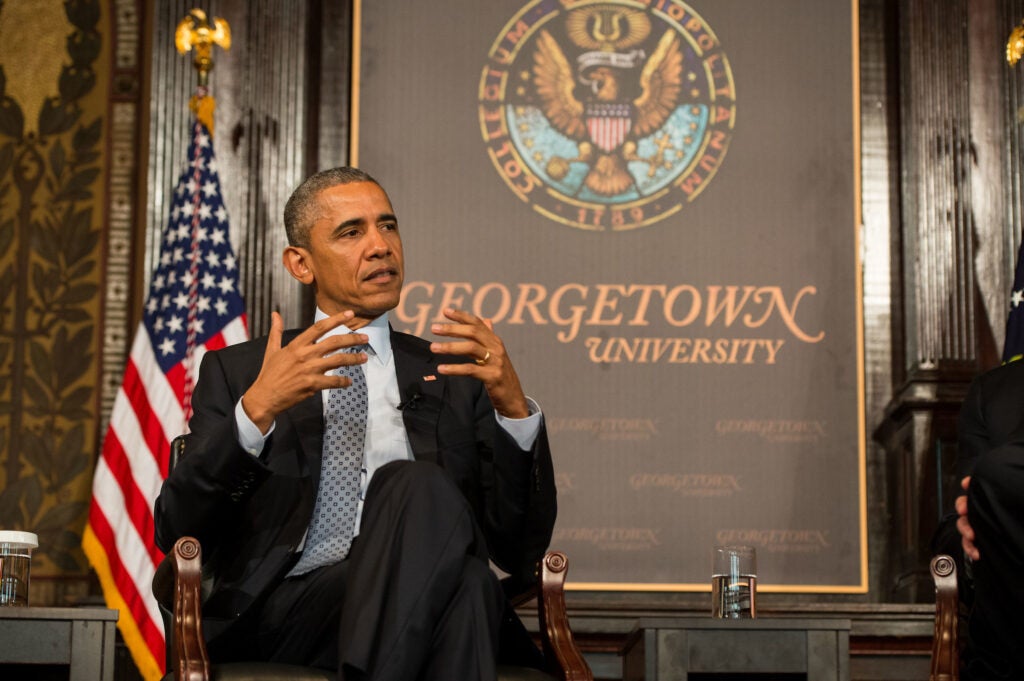 President Barack Obama sits in a chair in front of an American flag and Georgetown University sign at an event in Gaston Hall