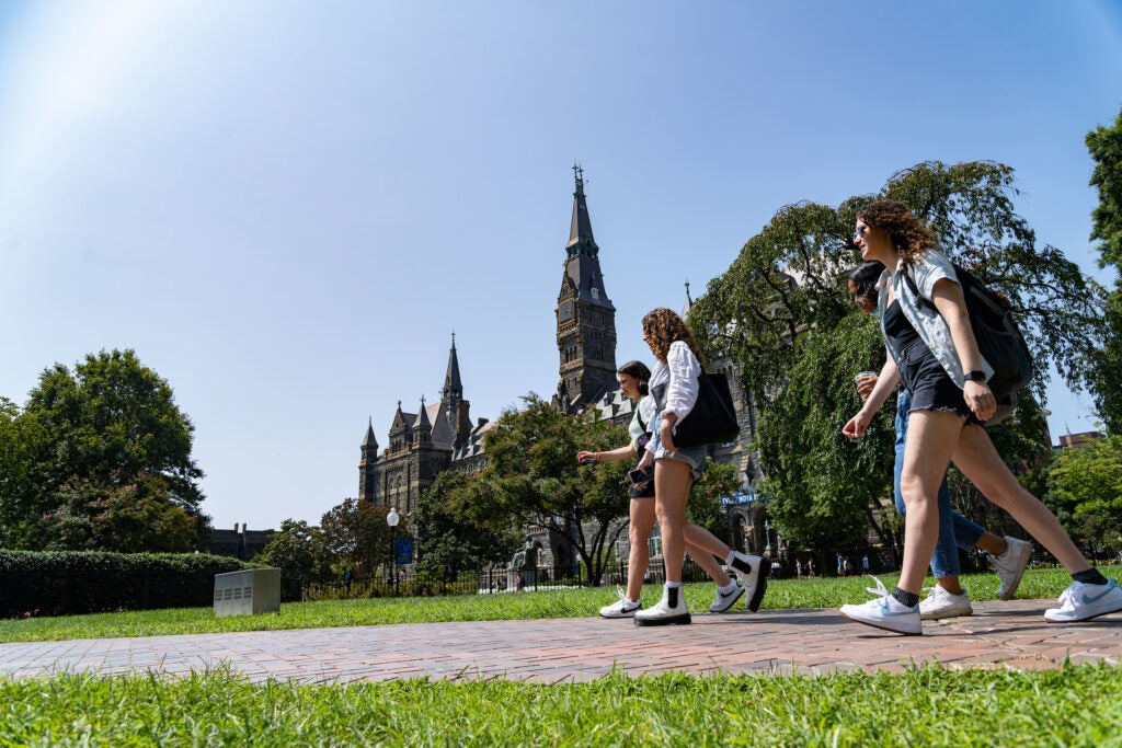 A group of Georgetown students walk on the path on Copley Lawn. Healy Hall can be seen in the distant background.