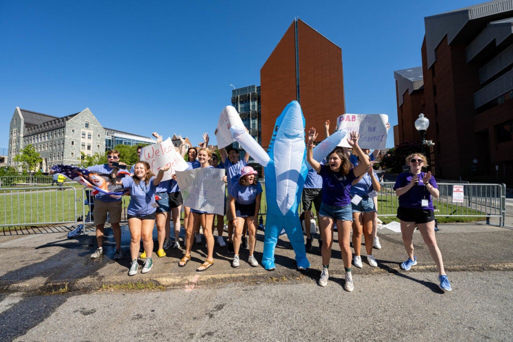 Students in matching T-shirts and a student dressed as a shark hold signs and cheer outside