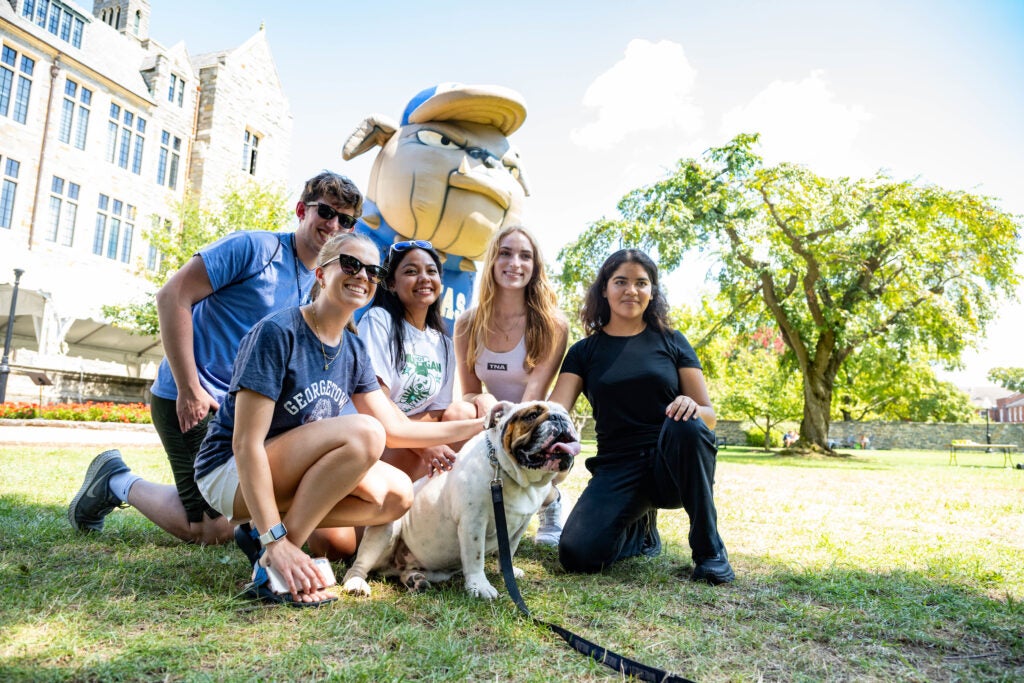 A group of Georgetown students pose for a photo with Jack the Bulldog outside on the Copley Lawn