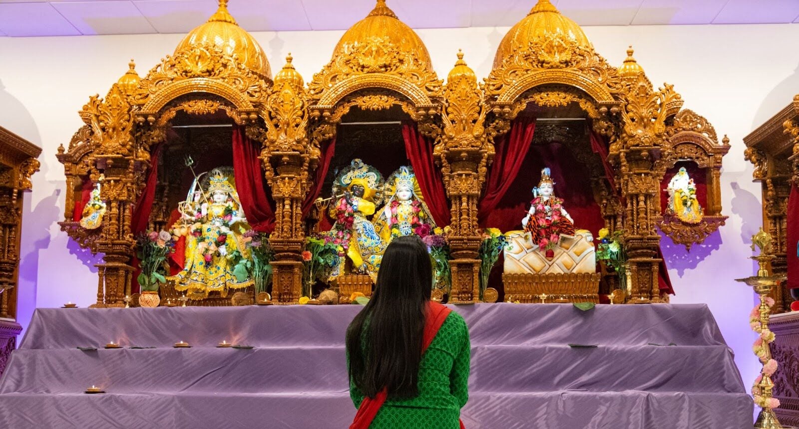 Woman sits wearing a green dress in front of an ornate gold shrine