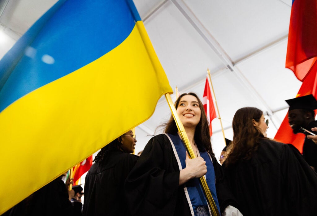 Young woman wearing graduation robes holds a Ukrainian flag