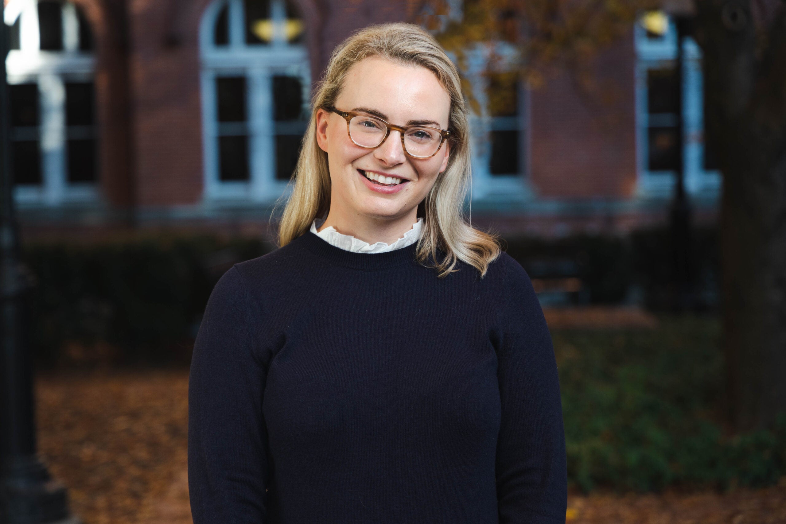 White woman with blonde hair and glasses wears a sweater while smiling at the camera