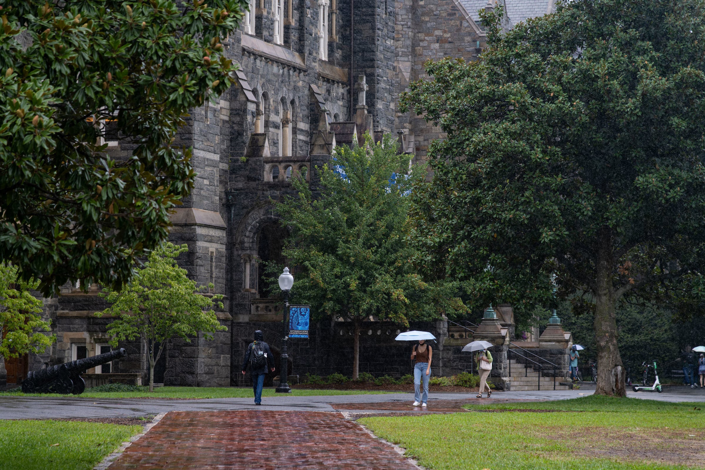 Students have umbrellas in front of Healy Hall in the rain